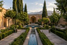 تصویری از محوطه سازی باغ سنتی با درختان متنوع و جوی آبی در وسط محوطه روان است.
